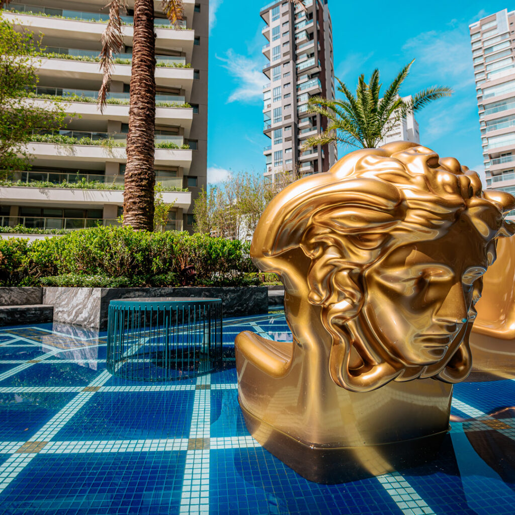 Piscina descoberta com escultura dourada do Villa Versace Moema. Foto do empreendimento pronto.